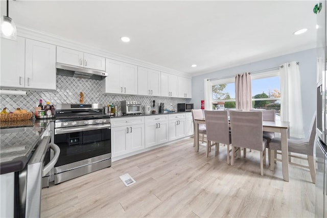 kitchen featuring appliances with stainless steel finishes, decorative light fixtures, decorative backsplash, white cabinets, and light wood-type flooring