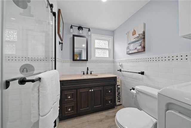 bathroom with vanity, a shower with door, hardwood / wood-style flooring, toilet, and tile walls