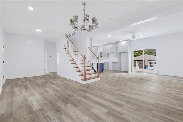 unfurnished living room featuring ceiling fan with notable chandelier and light wood-type flooring