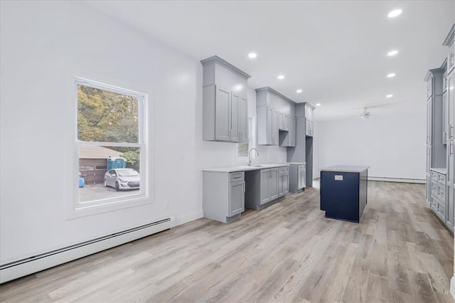 kitchen with gray cabinetry, sink, light hardwood / wood-style flooring, baseboard heating, and a kitchen island