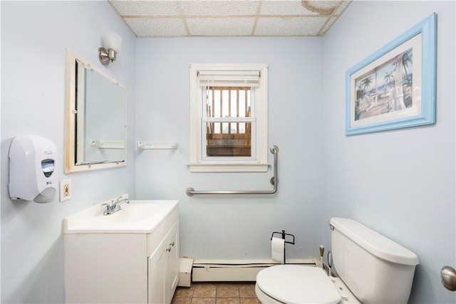 bathroom featuring a drop ceiling, vanity, a baseboard heating unit, tile patterned flooring, and toilet