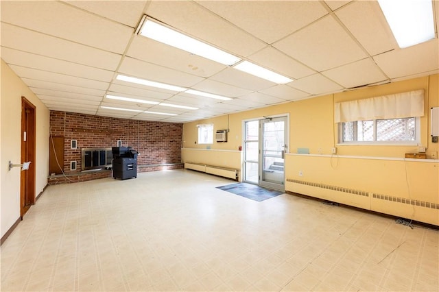 basement with a wall mounted AC, radiator heating unit, a drop ceiling, and a baseboard heating unit