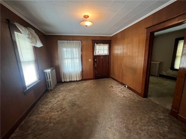 entryway with radiator, wood walls, crown molding, and dark carpet