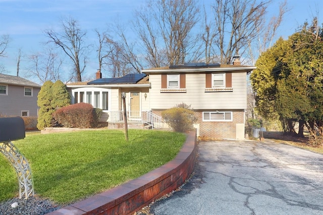 tri-level home featuring a front lawn and solar panels