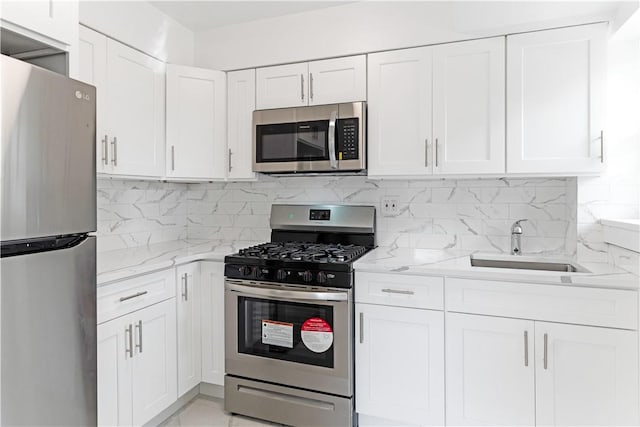 kitchen with light stone countertops, decorative backsplash, stainless steel appliances, sink, and white cabinets