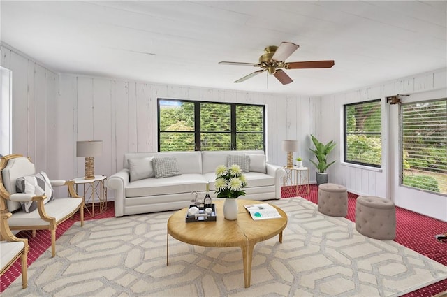 living room with wooden walls, ceiling fan, and a healthy amount of sunlight