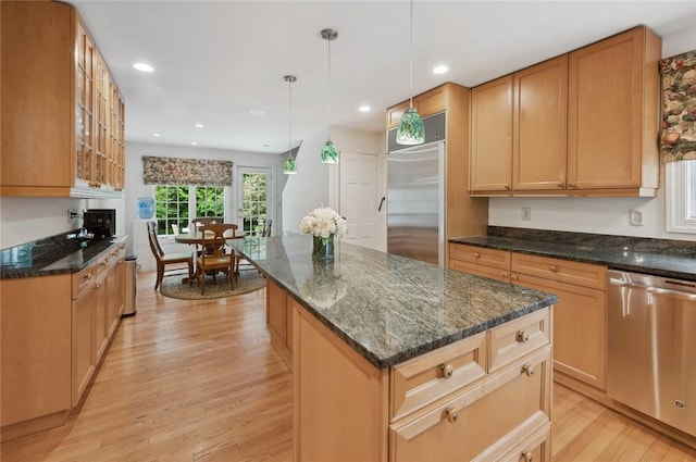 kitchen featuring appliances with stainless steel finishes, a center island, light hardwood / wood-style flooring, and dark stone countertops