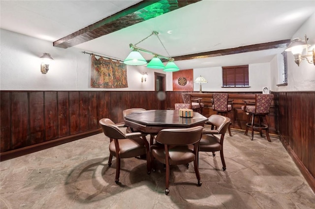 dining space featuring beamed ceiling, wood walls, and indoor bar