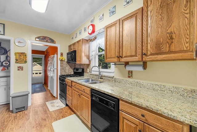 kitchen with light stone counters, ornamental molding, sink, black appliances, and light hardwood / wood-style floors