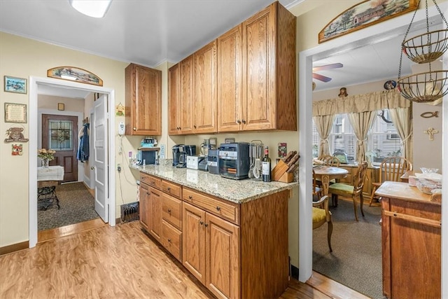 kitchen with ceiling fan, light hardwood / wood-style floors, light stone countertops, and ornamental molding