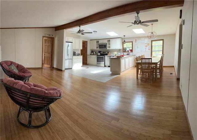 living room featuring ceiling fan, light hardwood / wood-style floors, beam ceiling, and a skylight