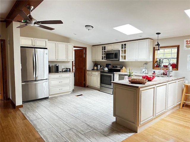 kitchen with stainless steel appliances, lofted ceiling with skylight, sink, pendant lighting, and light hardwood / wood-style flooring