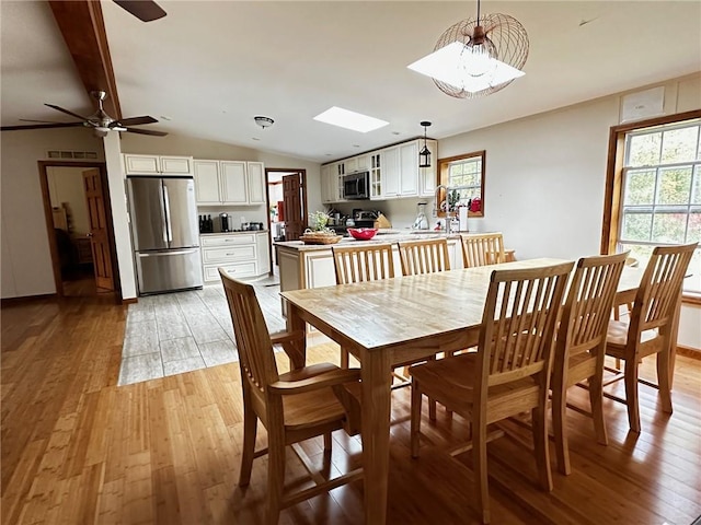 dining room featuring ceiling fan, light wood-type flooring, and lofted ceiling with skylight