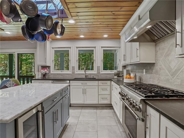 kitchen with white cabinets, wine cooler, high end stainless steel range, range hood, and tasteful backsplash