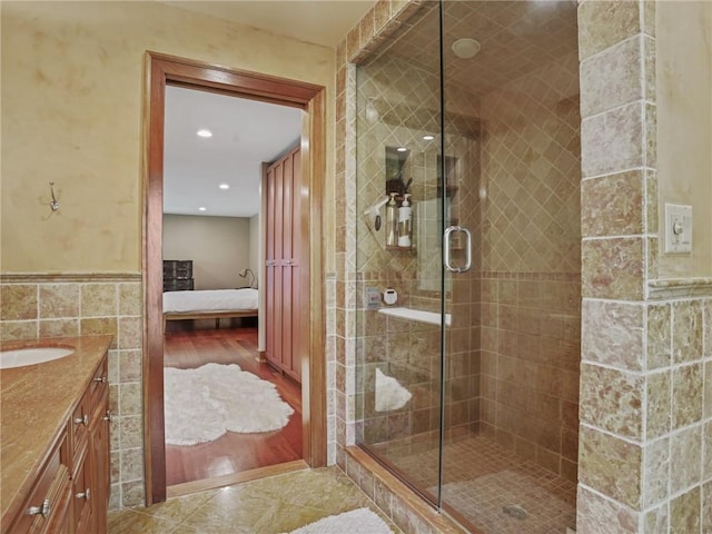 bathroom featuring vanity, wood-type flooring, a shower with door, and tile walls