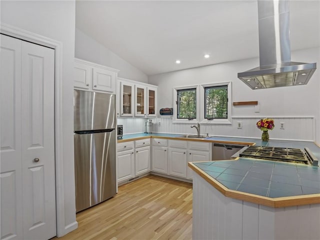 kitchen with tile countertops, white cabinets, island range hood, kitchen peninsula, and stainless steel appliances