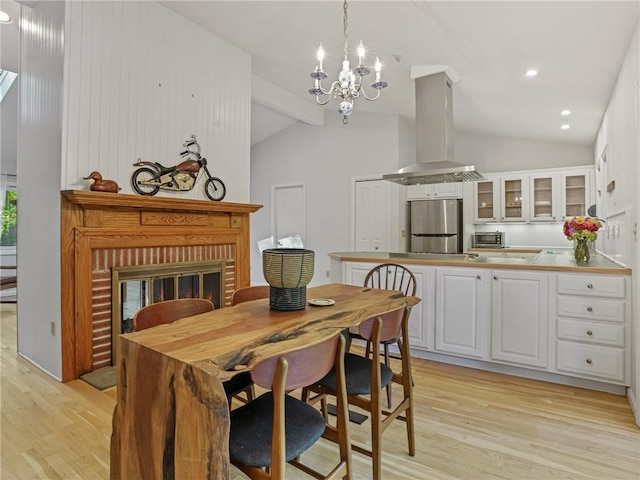 dining space with vaulted ceiling with beams, a fireplace, a notable chandelier, and light wood-type flooring