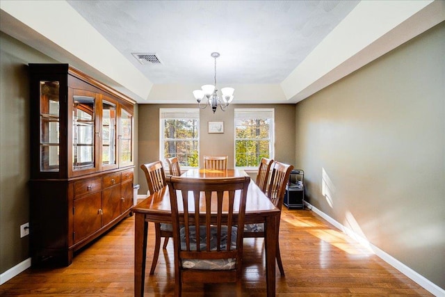 dining room with a tray ceiling, light hardwood / wood-style floors, and a notable chandelier