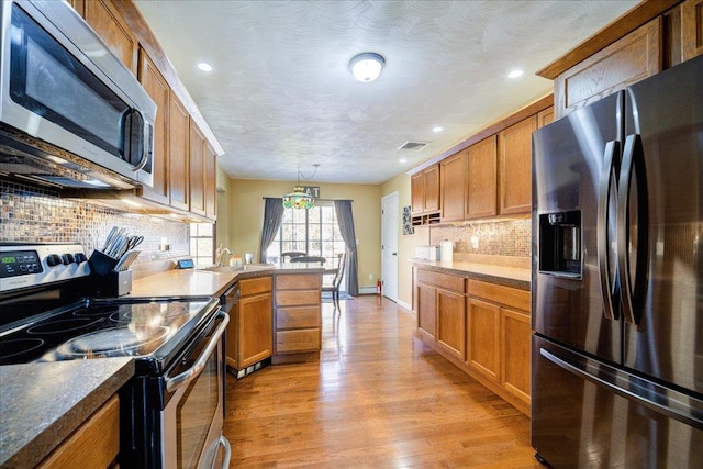 kitchen with light hardwood / wood-style flooring, decorative backsplash, a textured ceiling, decorative light fixtures, and stainless steel appliances