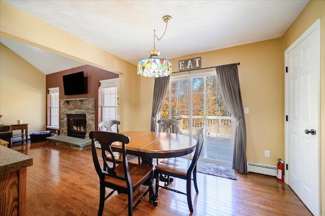 dining area featuring a fireplace, hardwood / wood-style floors, a baseboard radiator, and vaulted ceiling