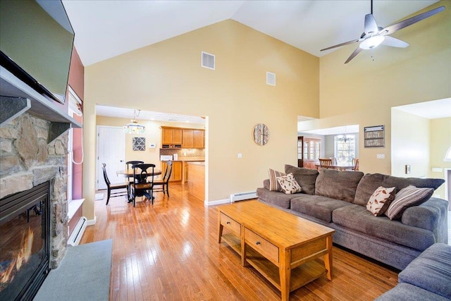 living room featuring ceiling fan, a baseboard radiator, a stone fireplace, high vaulted ceiling, and light hardwood / wood-style floors