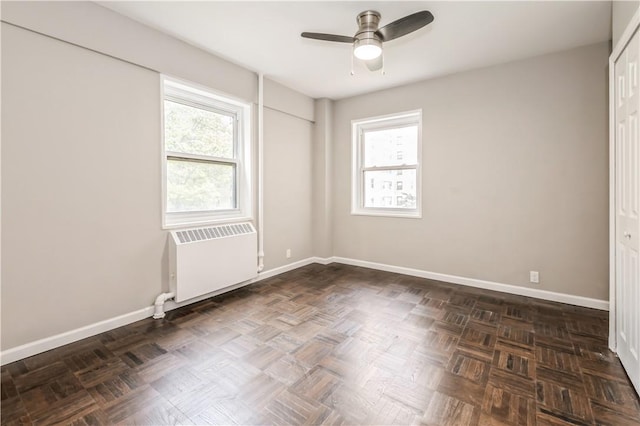 unfurnished room featuring dark parquet flooring, plenty of natural light, radiator, and ceiling fan