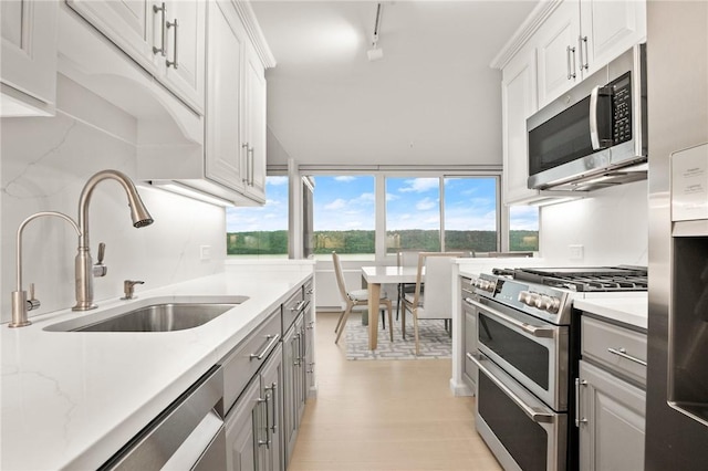 kitchen with light stone countertops, appliances with stainless steel finishes, light wood-type flooring, sink, and white cabinets