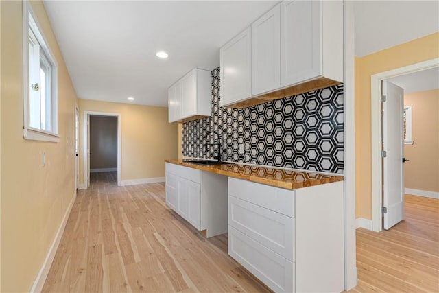 kitchen with decorative backsplash, light hardwood / wood-style flooring, white cabinetry, and wood counters