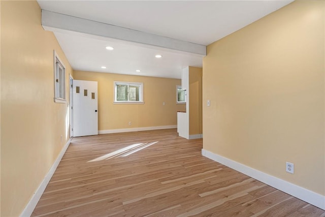 spare room with beam ceiling and light hardwood / wood-style flooring