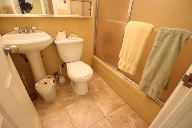 bathroom featuring tile patterned floors, combined bath / shower with glass door, decorative backsplash, toilet, and tile walls