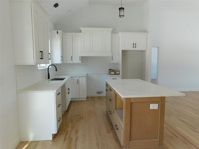 kitchen with sink, decorative light fixtures, white cabinetry, a kitchen island, and decorative backsplash