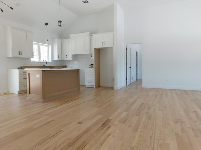 kitchen featuring light hardwood / wood-style floors, tasteful backsplash, white cabinets, a kitchen island, and decorative light fixtures