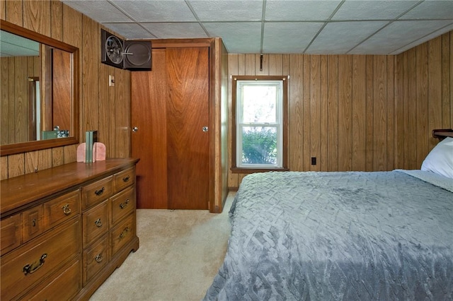 bedroom featuring light carpet, a paneled ceiling, a closet, and wood walls