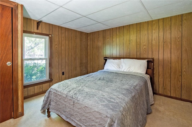 bedroom with a paneled ceiling, light carpet, and wooden walls