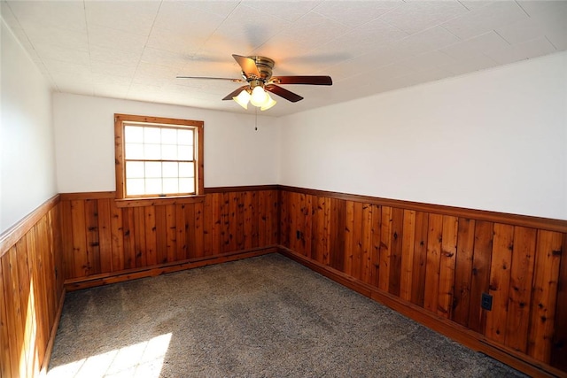 empty room with wooden walls, carpet floors, and ceiling fan