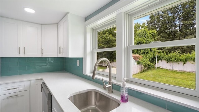 kitchen with stainless steel dishwasher, decorative backsplash, white cabinetry, and sink