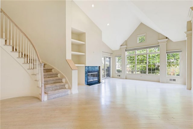 unfurnished living room with a fireplace, light wood-type flooring, high vaulted ceiling, and built in features