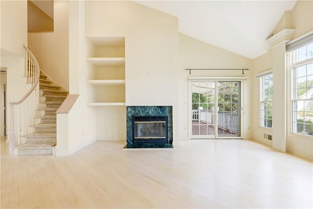 unfurnished living room featuring hardwood / wood-style floors, built in features, a fireplace, and high vaulted ceiling