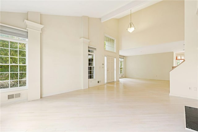 unfurnished living room with beamed ceiling, plenty of natural light, and light hardwood / wood-style flooring