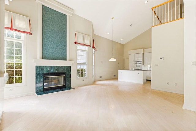 unfurnished living room with a premium fireplace, high vaulted ceiling, and light hardwood / wood-style floors