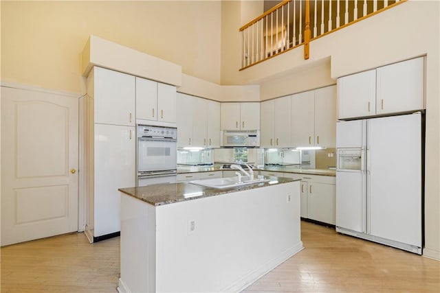 kitchen featuring light wood-type flooring, white appliances, dark stone countertops, a high ceiling, and white cabinetry