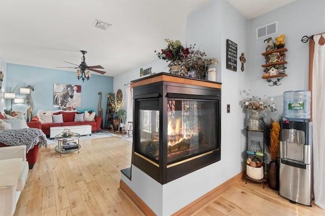 living room featuring a multi sided fireplace, ceiling fan, and light wood-type flooring