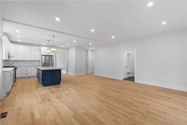 kitchen with appliances with stainless steel finishes, light hardwood / wood-style flooring, white cabinets, a kitchen island, and hanging light fixtures