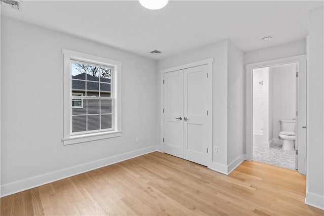 unfurnished bedroom featuring ensuite bath, a closet, and light hardwood / wood-style flooring