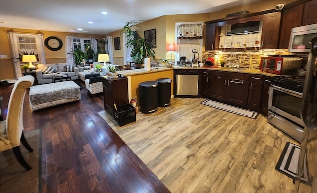 kitchen with dark brown cabinets, light wood-type flooring, stainless steel appliances, and tasteful backsplash