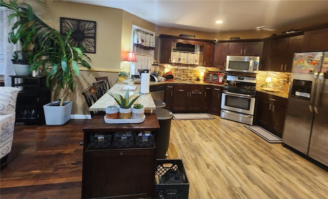 kitchen with dark brown cabinets, backsplash, stainless steel appliances, and light hardwood / wood-style flooring