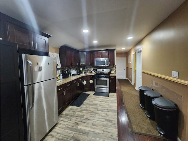 kitchen featuring dark brown cabinets, light wood-type flooring, backsplash, and appliances with stainless steel finishes