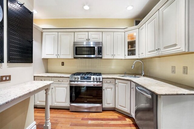 kitchen with light stone countertops, light wood-type flooring, stainless steel appliances, sink, and white cabinetry