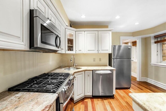 kitchen with white cabinets, sink, light hardwood / wood-style flooring, light stone counters, and stainless steel appliances