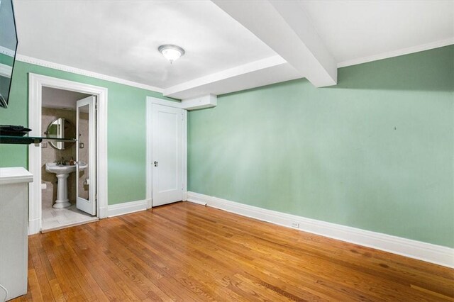 unfurnished bedroom featuring ensuite bath, sink, beamed ceiling, crown molding, and wood-type flooring